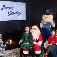 Girl in sparkling green dress sits on Santa's lap while brother sits on mom